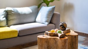 Una sala de estar con sofá, cojines, una mesa de centro de madera y una planta en maceta.