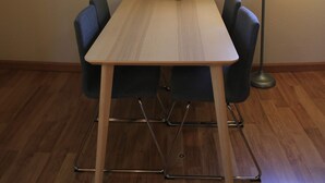Un comedor con una mesa de madera y cuatro sillas, una obra de arte enmarcada en la pared y una lámpara de pie.