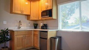 Cocina compacta con muebles de madera, lavavajillas de acero inoxidable y ventana con persianas.