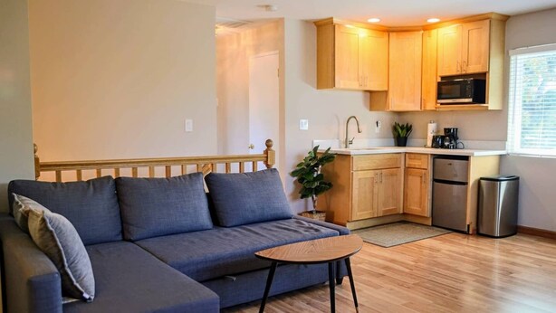 Una sala de estar moderna con un sofá, una mesita y una cocina con armarios de madera y electrodomésticos.