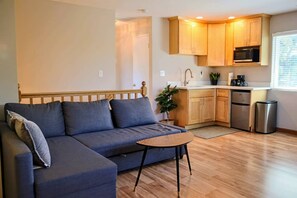 Un salon moderne comprenant un canapé, une petite table et un coin cuisine avec des meubles et des appareils électroménagers en bois.