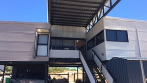 A modern building with a metal roof, multiple windows, and a staircase leading to an upper level.