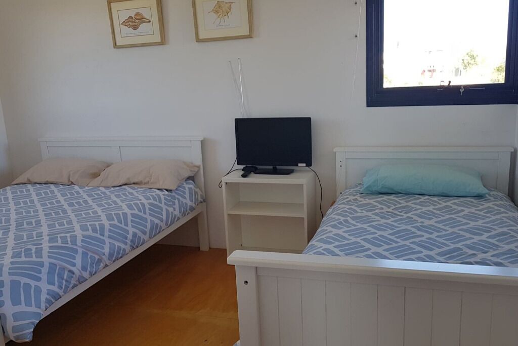 A bedroom with two single beds, a TV on a stand, and framed pictures on the wall.