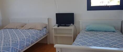 A bedroom with two single beds, a TV on a stand, and framed pictures on the wall.