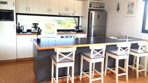 A modern kitchen with white cabinets, a central island with bar stools, a refrigerator, and a window with a view of greenery.
