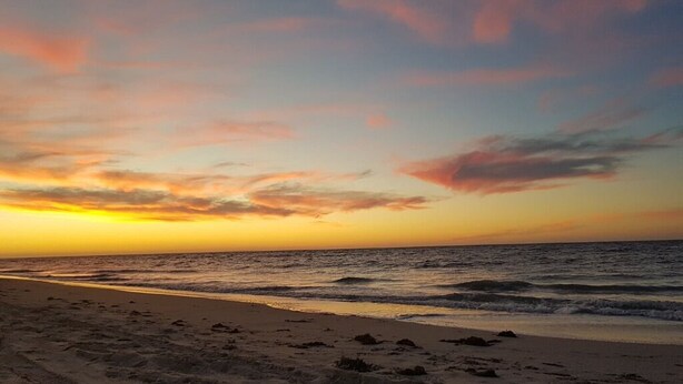 A beach at sunset with a clear sky and calm sea.