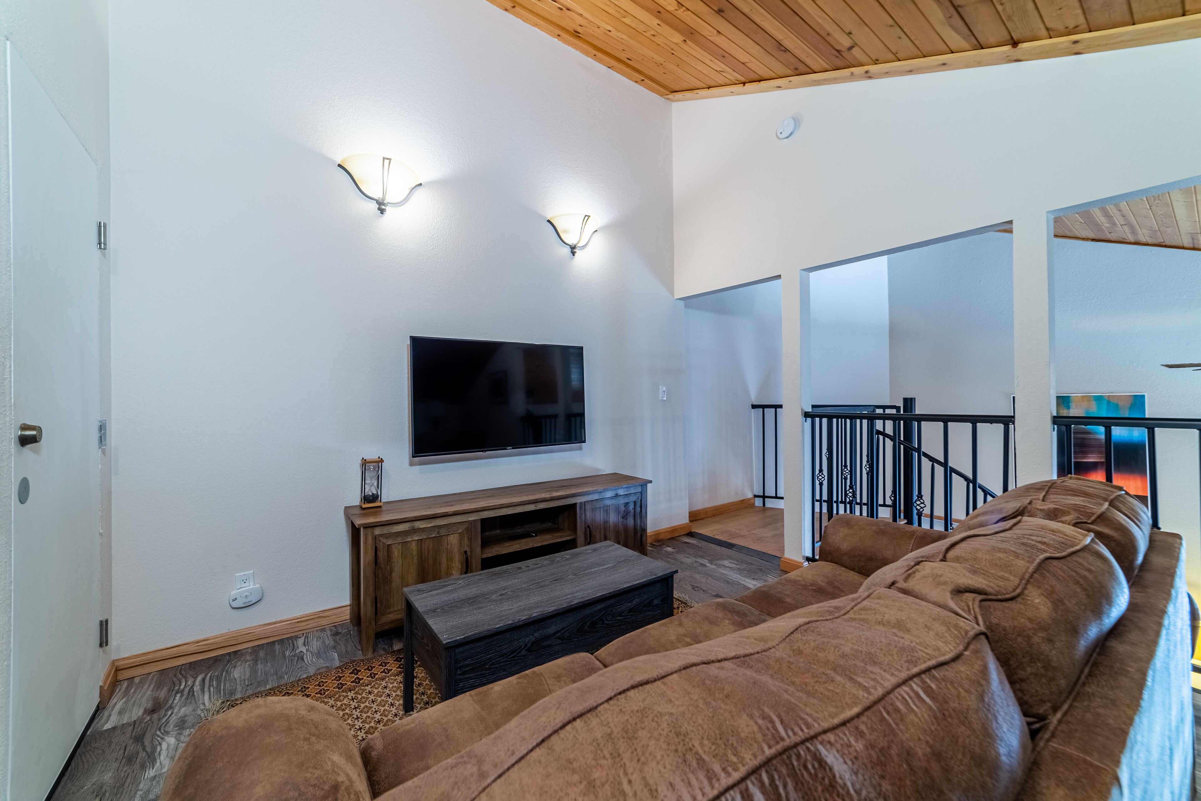 A spacious living room with a large sectional sofa, a flat-screen TV, wooden entertainment unit, and a staircase leading to another level.
