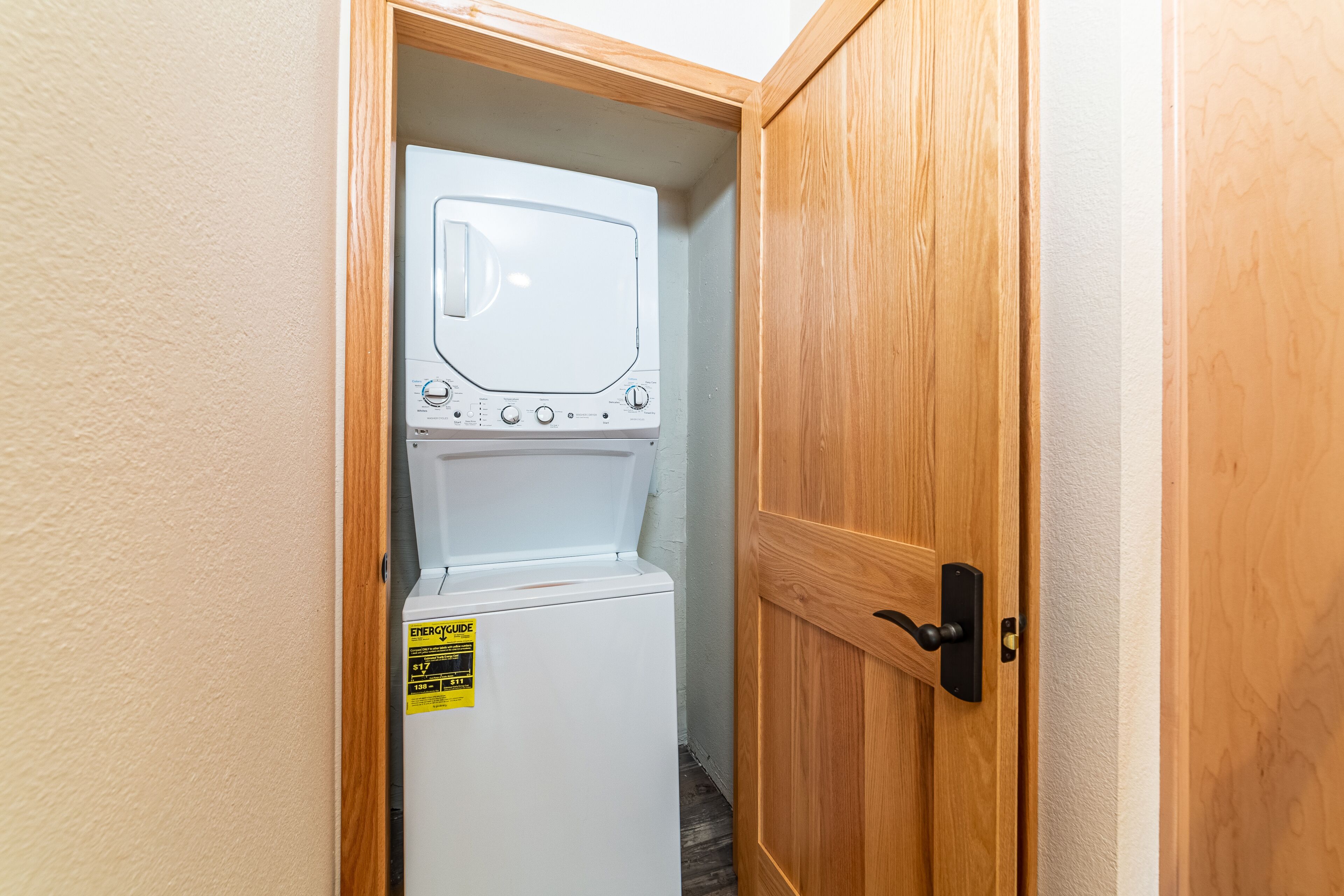 A compact laundry room with a front-loading washer and dryer, wooden door, and a small sign on the dryer.
