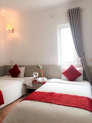 A hotel room with two beds, each with red and white bedding, a small table with a vase of flowers, and a window with curtains. - The Carnation Hotel Da Nang (Da Nang)