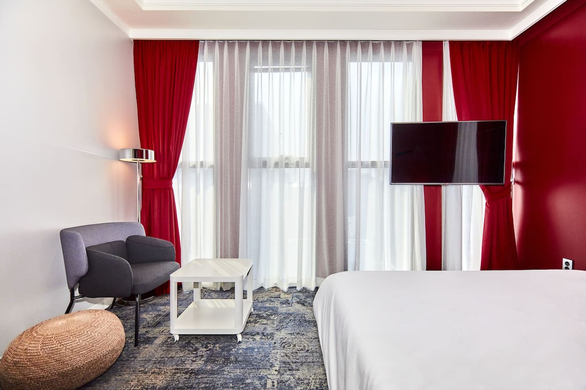 A hotel room with a bed, a desk, a chair, a TV, and a window with curtains.