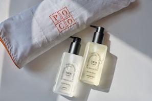 Toalla blanca con 'POCO' bordado en rojo, dos botellas de champú de 'KOLON HOTEL' y un dispensador de gel de ducha 'SW19 Still Moon'.