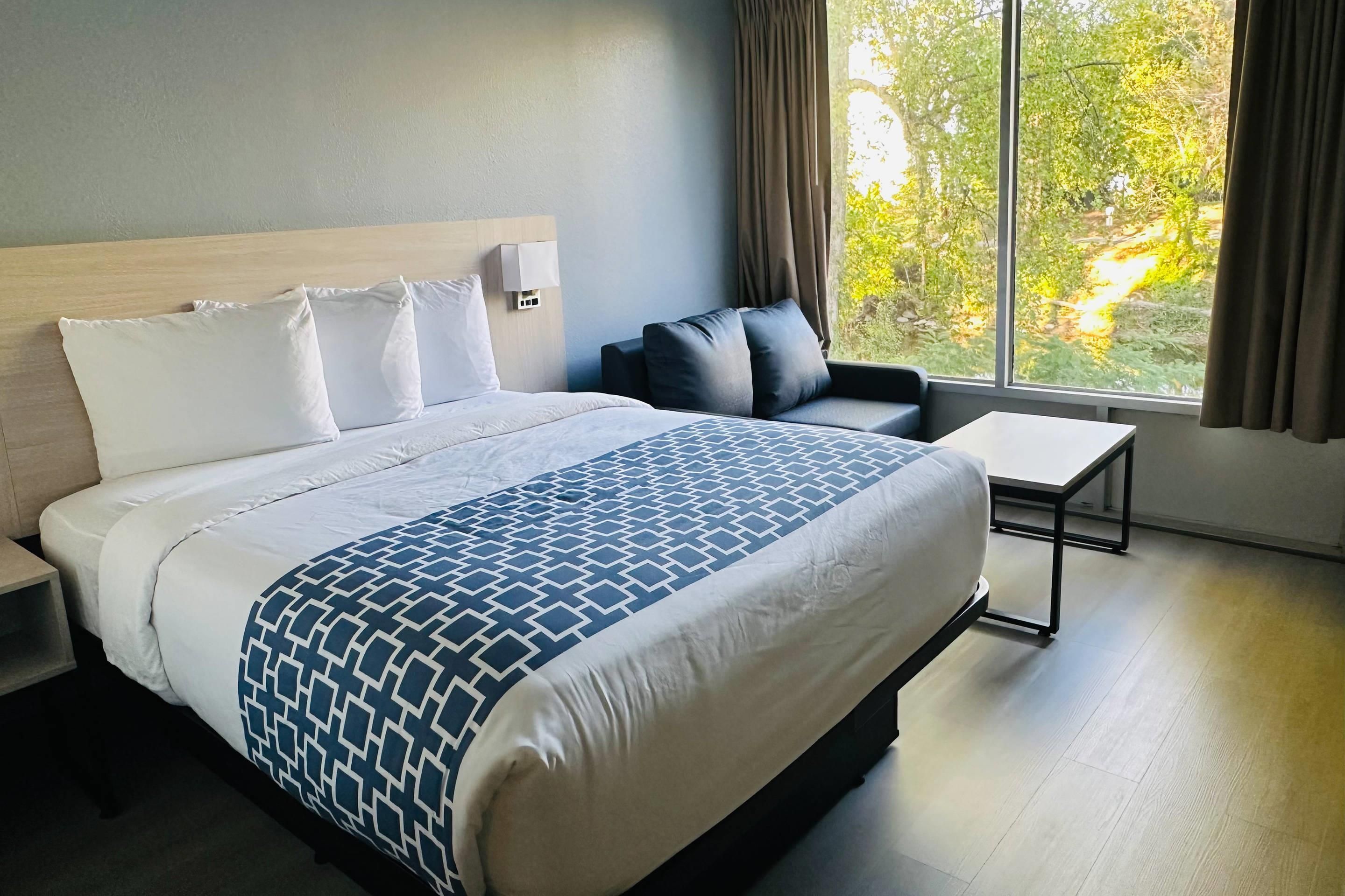 Una camera d'albergo con un letto grande, un comodino, una sedia e una finestra con tende.