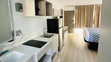 Una camera d'albergo compatta con angolo cottura, un letto con biancheria a motivi decorativi e un bagno con doccia.