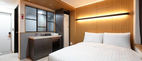 A hotel room with a bed, a vanity with a mirror, and a wall-mounted light fixture.