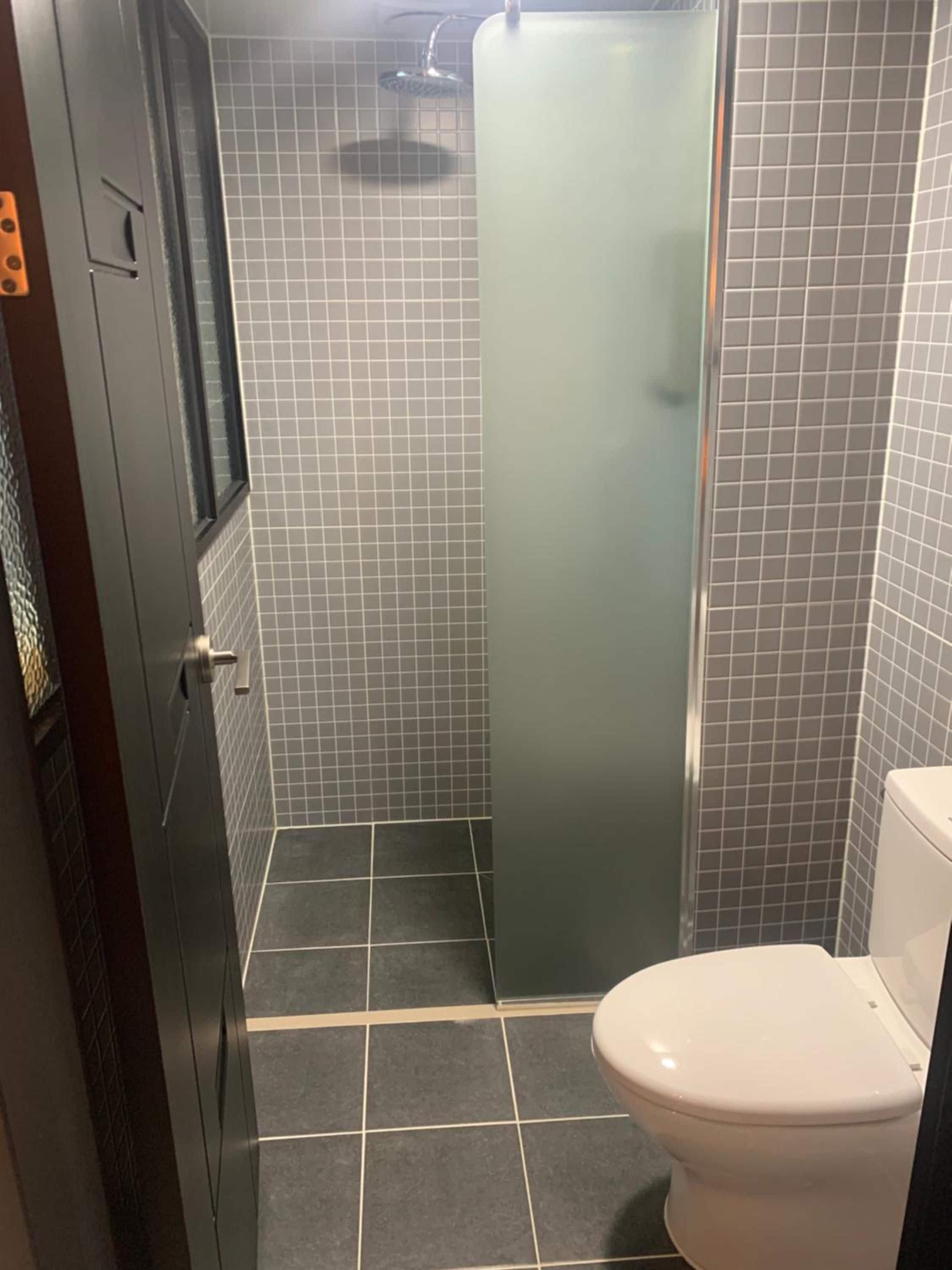 Een badkamer met toilet, douchecabine en betegelde wanden.