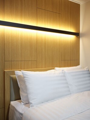 A neatly made bed with white linens and pillows, a wooden headboard, and a horizontal light strip above the bed. - S Stay Hotel (Suwon)