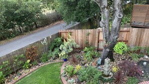 Een tuin met verschillende planten, een kleine fontein en een houten omheining.