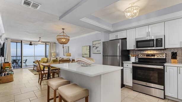A modern kitchen with white cabinetry, stainless steel appliances, and a central island with bar stools. - Top-Floor Gulf Views | Updated Condo Near Beach & Times Square & Pool Access (Fort Myers Beach)