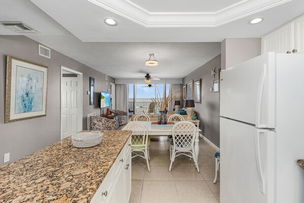 A kitchen with a granite countertop, white chairs, a dining table, and a white refrigerator.