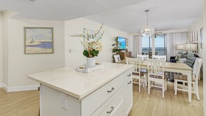 A modern kitchen with white cabinetry, a central island, and a dining area with white chairs.