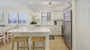 A modern kitchen with white cabinetry, a large island with stools, a stainless steel refrigerator, and a ceiling light fixture.