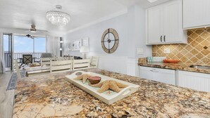 A spacious living area with a large marble island, a ceiling fan, and a decorative wall clock. - Gulf-Front Condo | Heated Pool, Beach Access & Walk to Times Square (Fort Myers Beach)