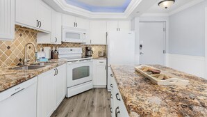 A modern kitchen with white cabinets, a Bosch oven, a microwave, and a granite countertop. - Gulf-Front Condo | Heated Pool, Beach Access & Walk to Times Square (Fort Myers Beach)