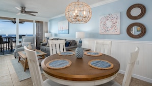 Un comedor con una mesa de madera redonda, sillas blancas y individuales de tejido azul.