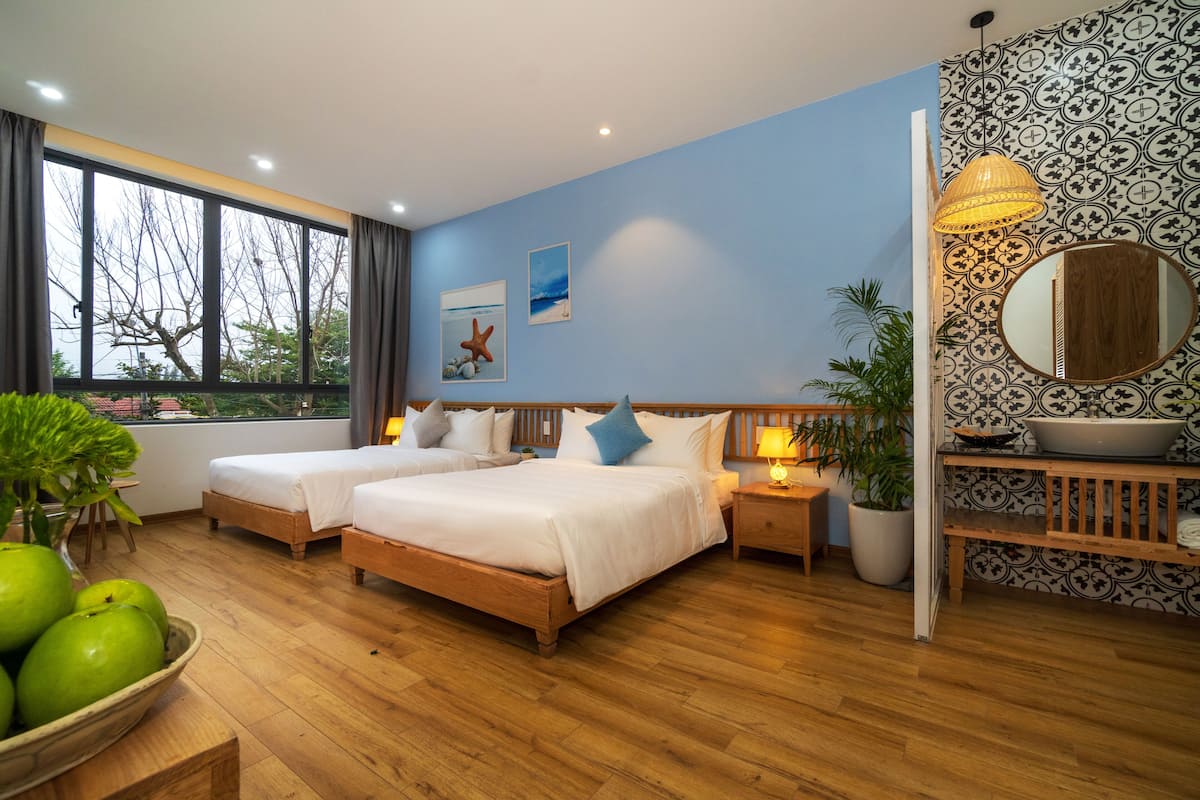 A hotel room with two beds, a large window, a potted plant, and a decorative mirror.