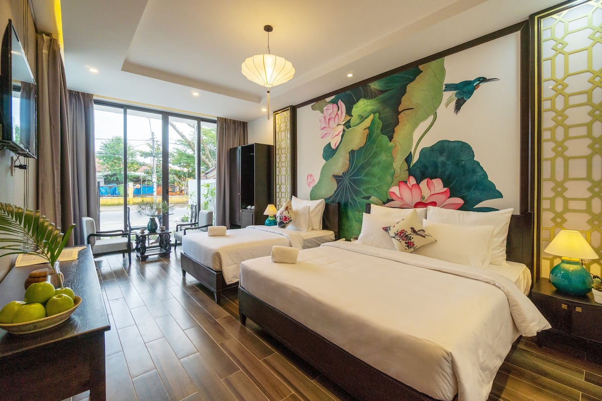 A hotel room with two beds, a dining table, and a large window.