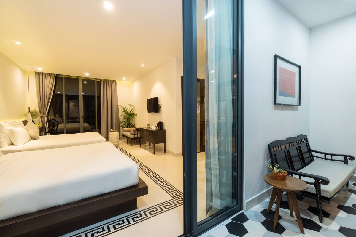 A modern hotel room with two beds, a sofa, a small table, and a TV.