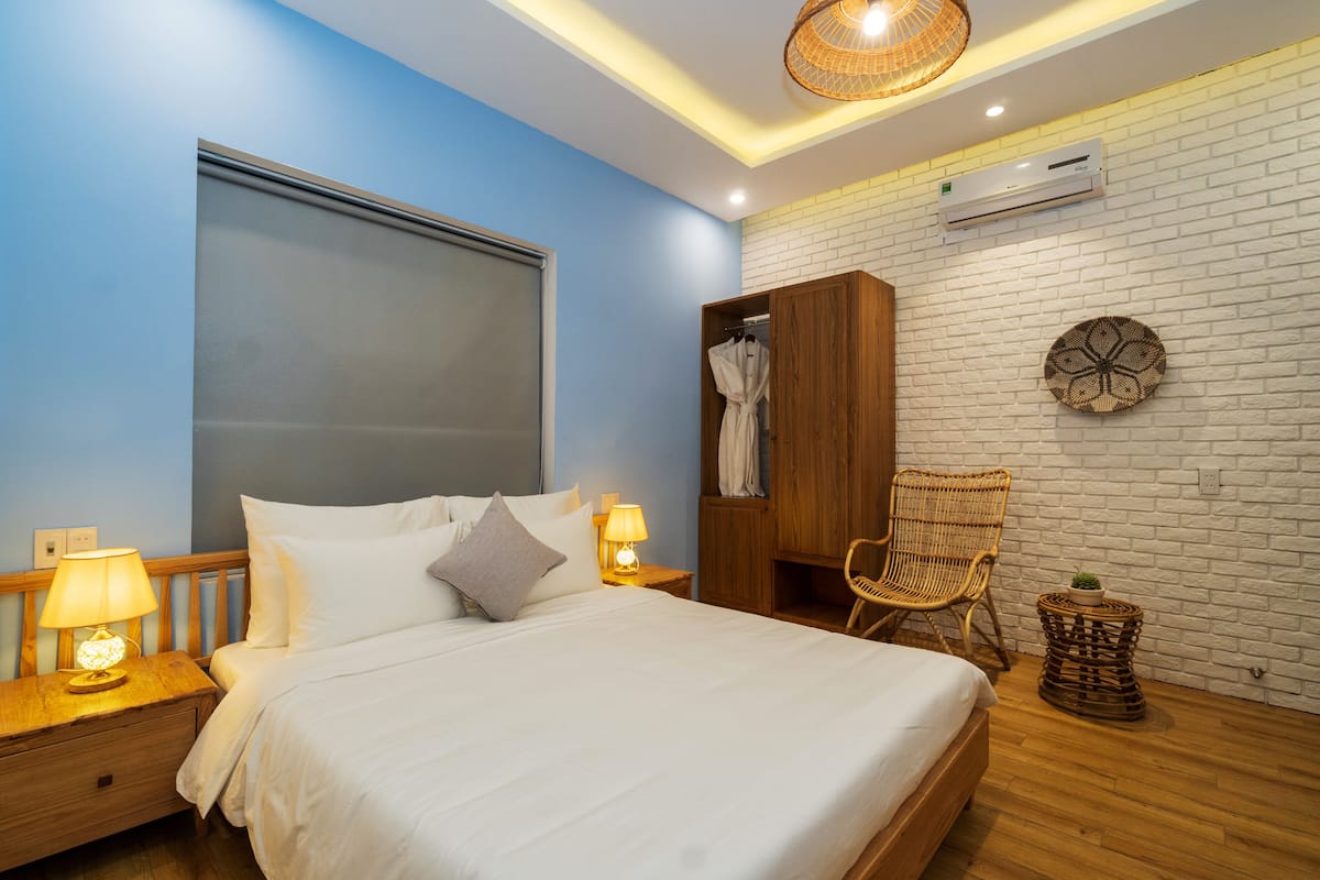 A bedroom with a bed, nightstands, a wardrobe, a wicker chair, and a small table with a plant.