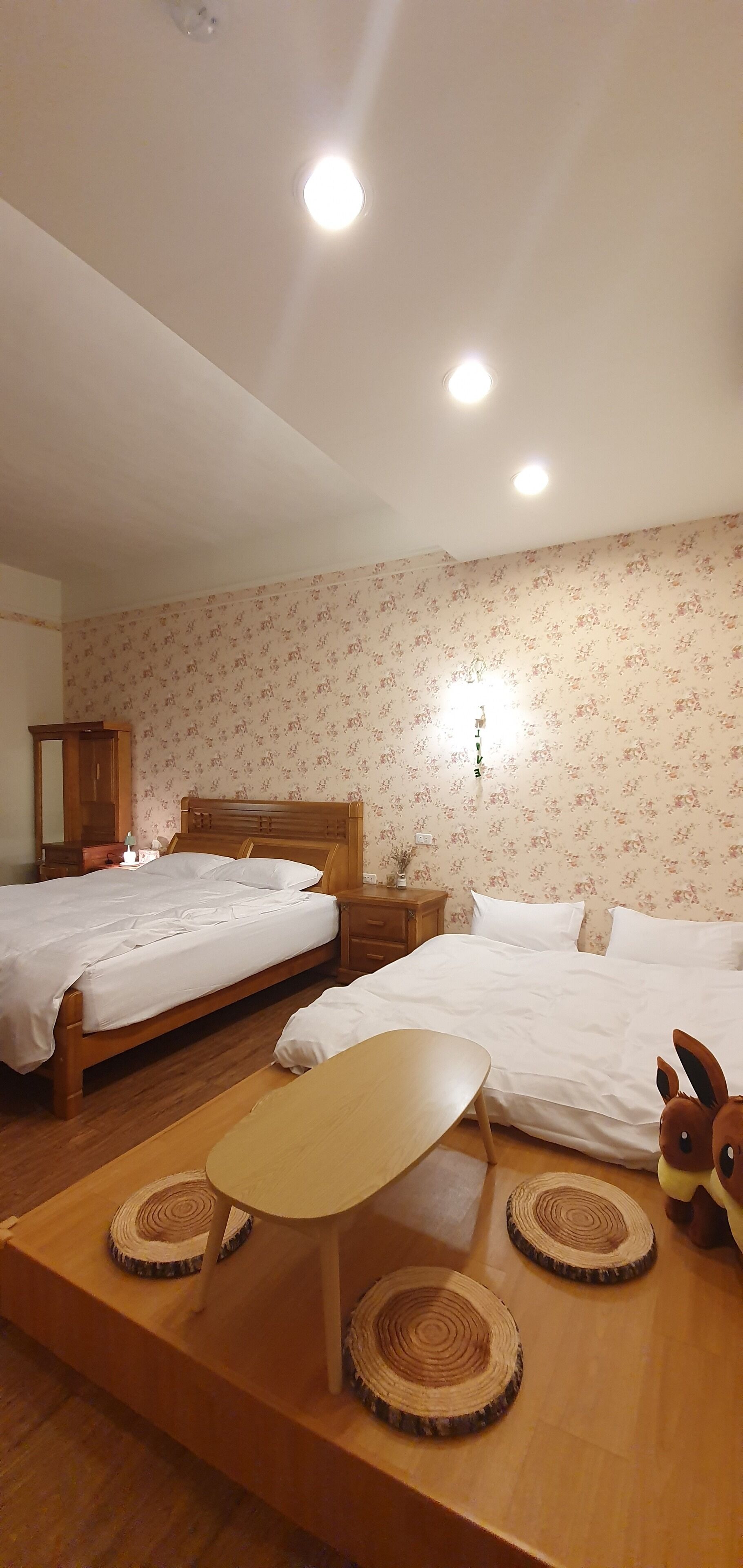 A hotel room with two beds, a wooden table, and a small table lamp.