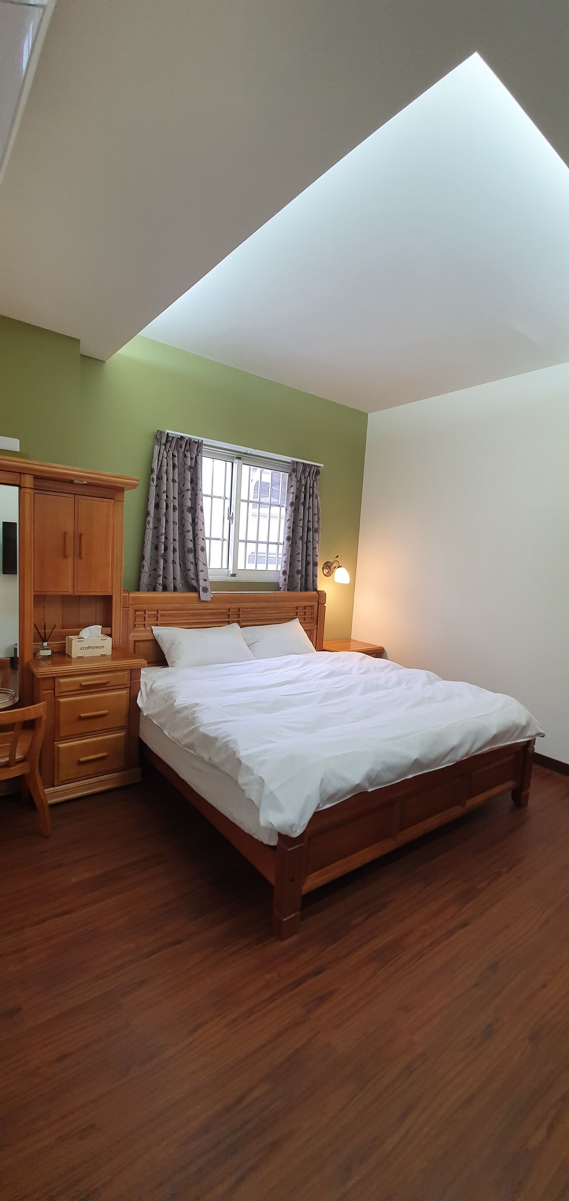 A bedroom with a wooden bed, a nightstand, a wooden dresser, and a window with curtains.
