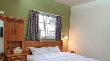A bedroom with a wooden bed, a nightstand, a wooden dresser, and a window with curtains.