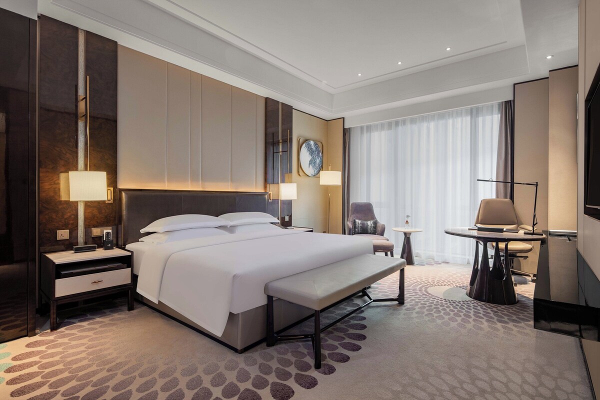 A modern hotel room with a large bed, bedside tables, a desk, and a chair.