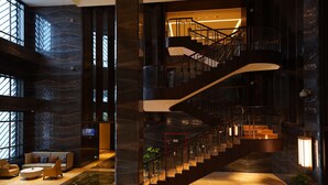 A modern hotel lobby with a curved staircase, seating area, and large windows. - Haikou Yatter Hotel, Vignette Collection by IHG (Haikou)