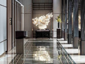 A modern lobby with a reflective marble floor, a central decorative sculpture, and a potted plant. - Haikou Yatter Hotel, Vignette Collection by IHG (Haikou)