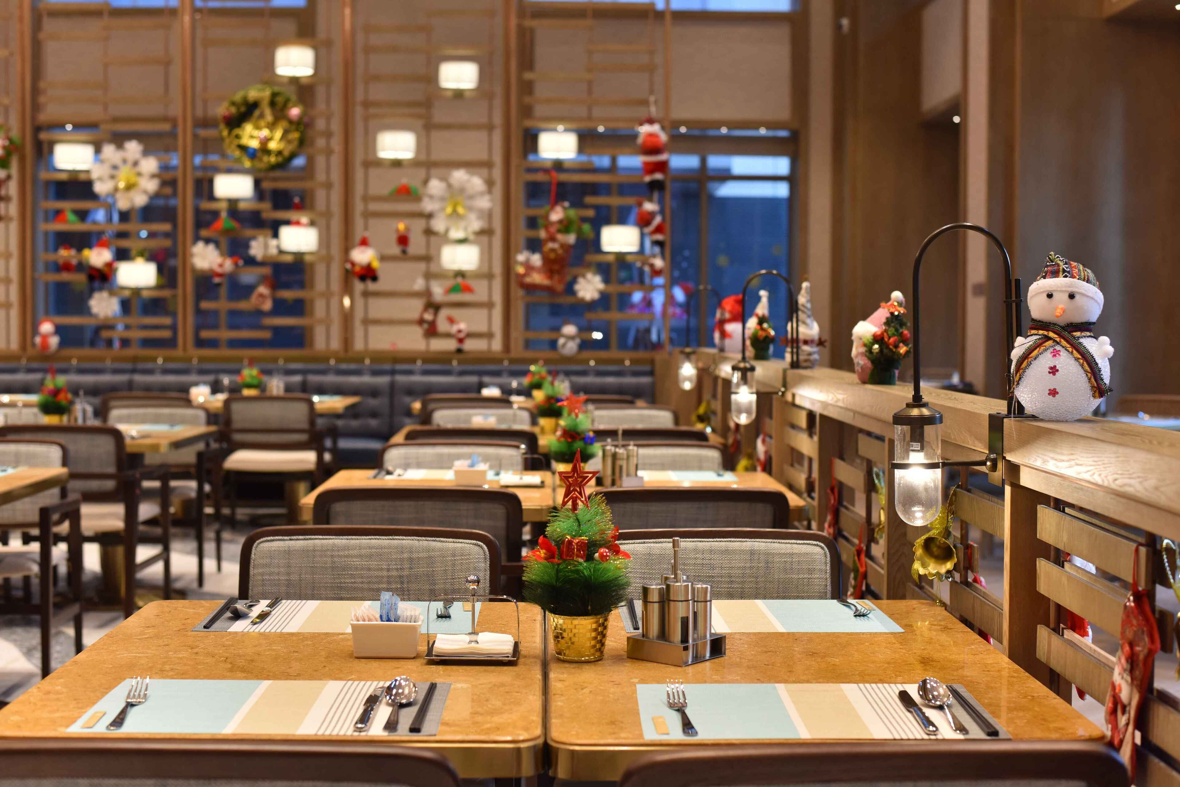 A hotel dining area with neatly arranged tables, each with a placemat, cutlery, and a small decorative tree.