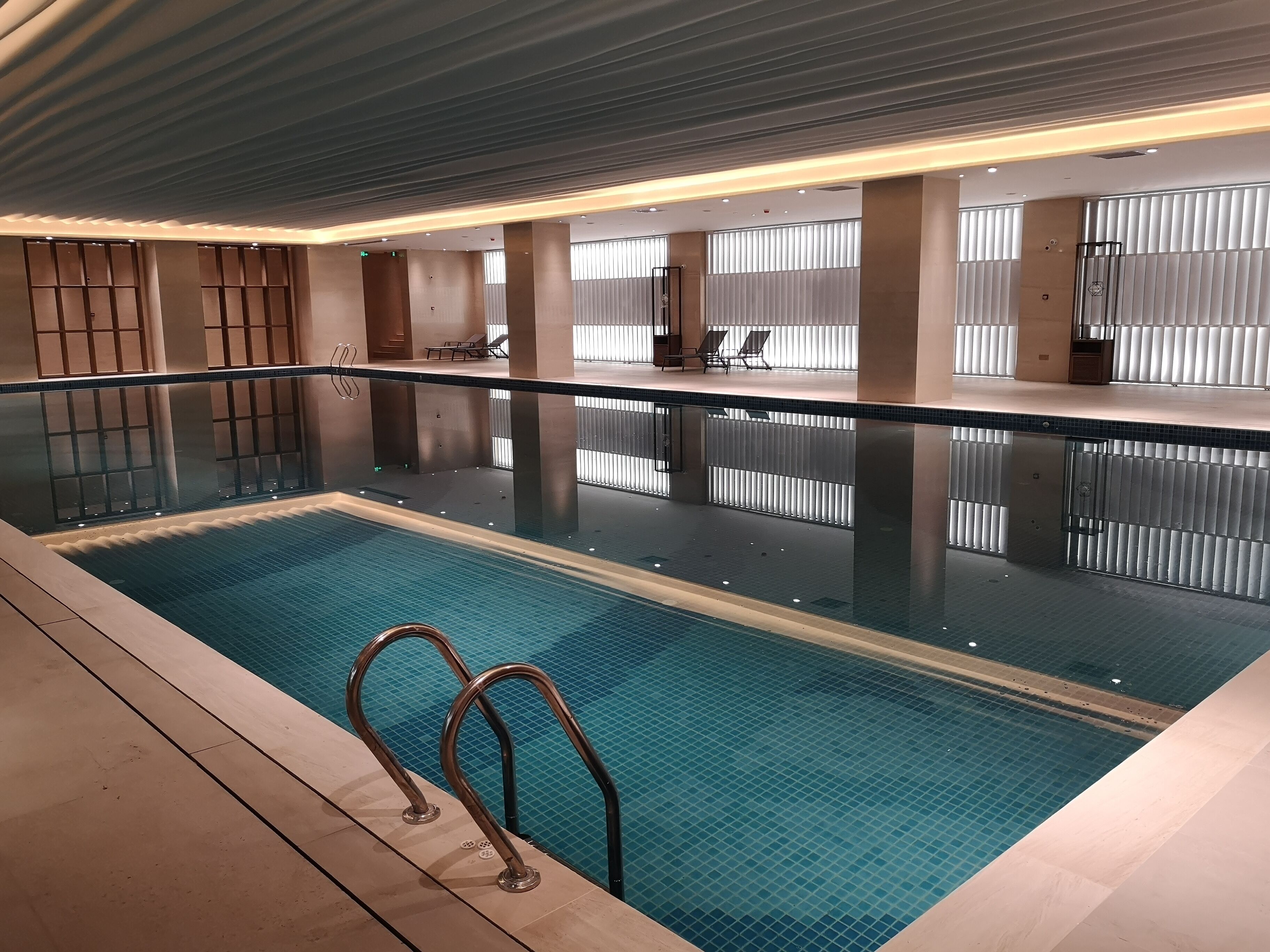 Una piscina interior con agua cristalina, barandales de metal y suelo de baldosas.