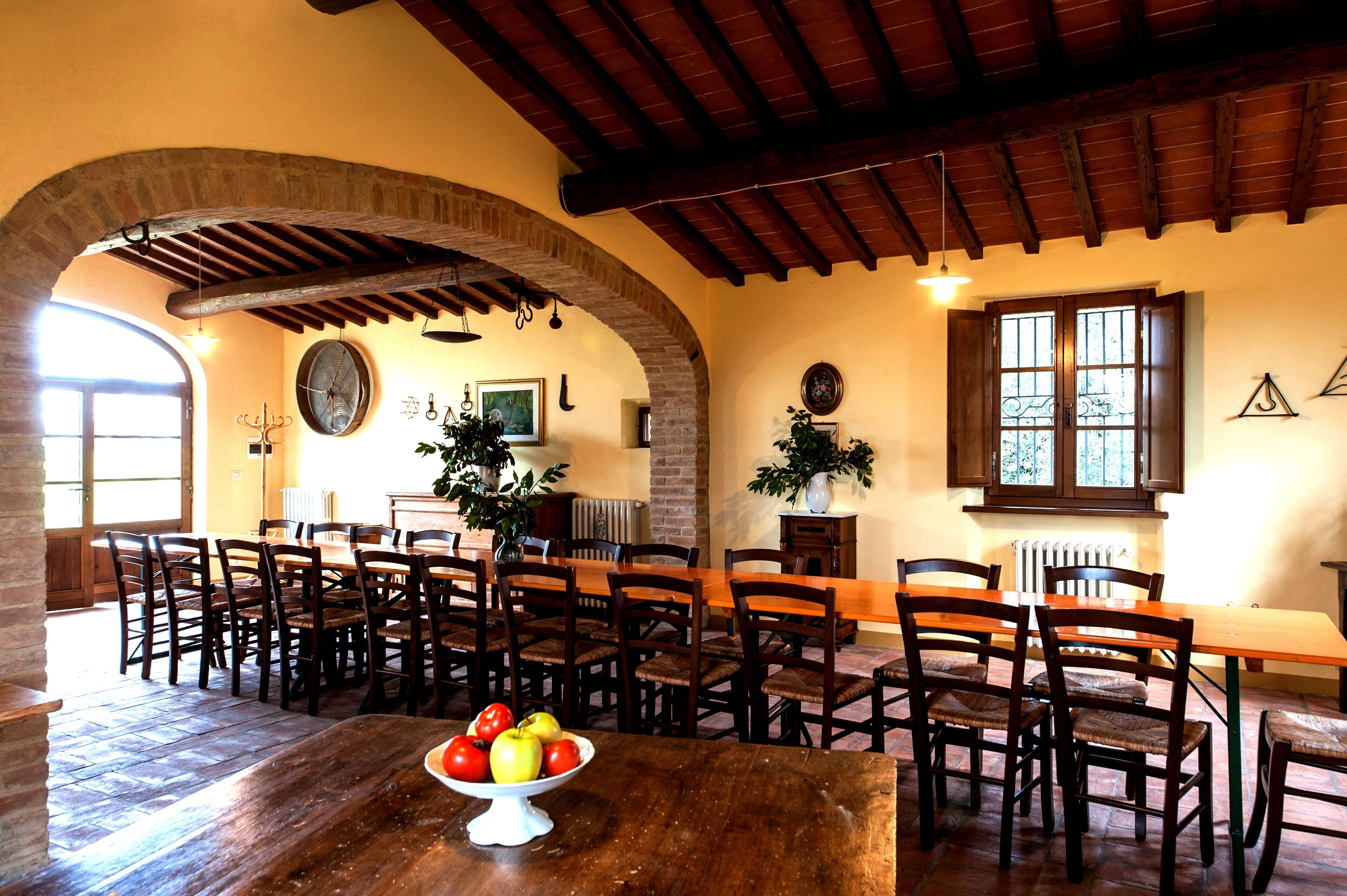 Un comedor con una larga mesa de madera y sillas, un cuenco de fruta sobre la mesa y un rústico arco de ladrillo.