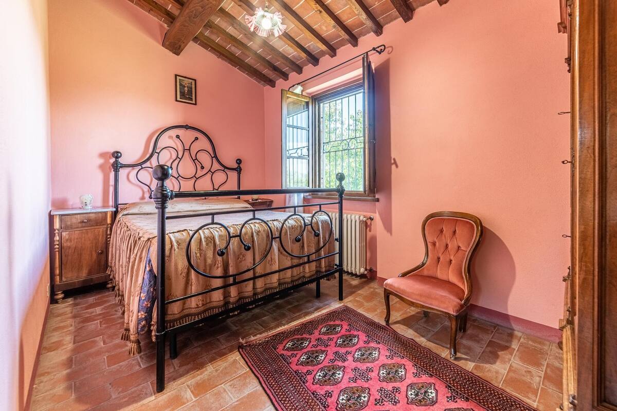 A bedroom with a metal bed frame, a wooden chair, a radiator, and a window with bars.