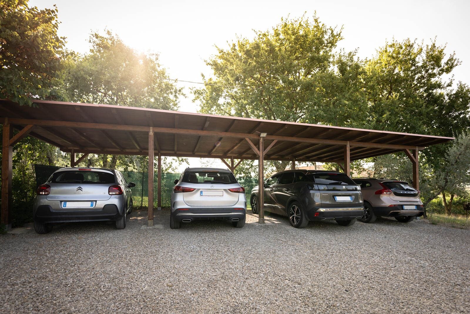 Three cars parked under a covered area with trees in the background.