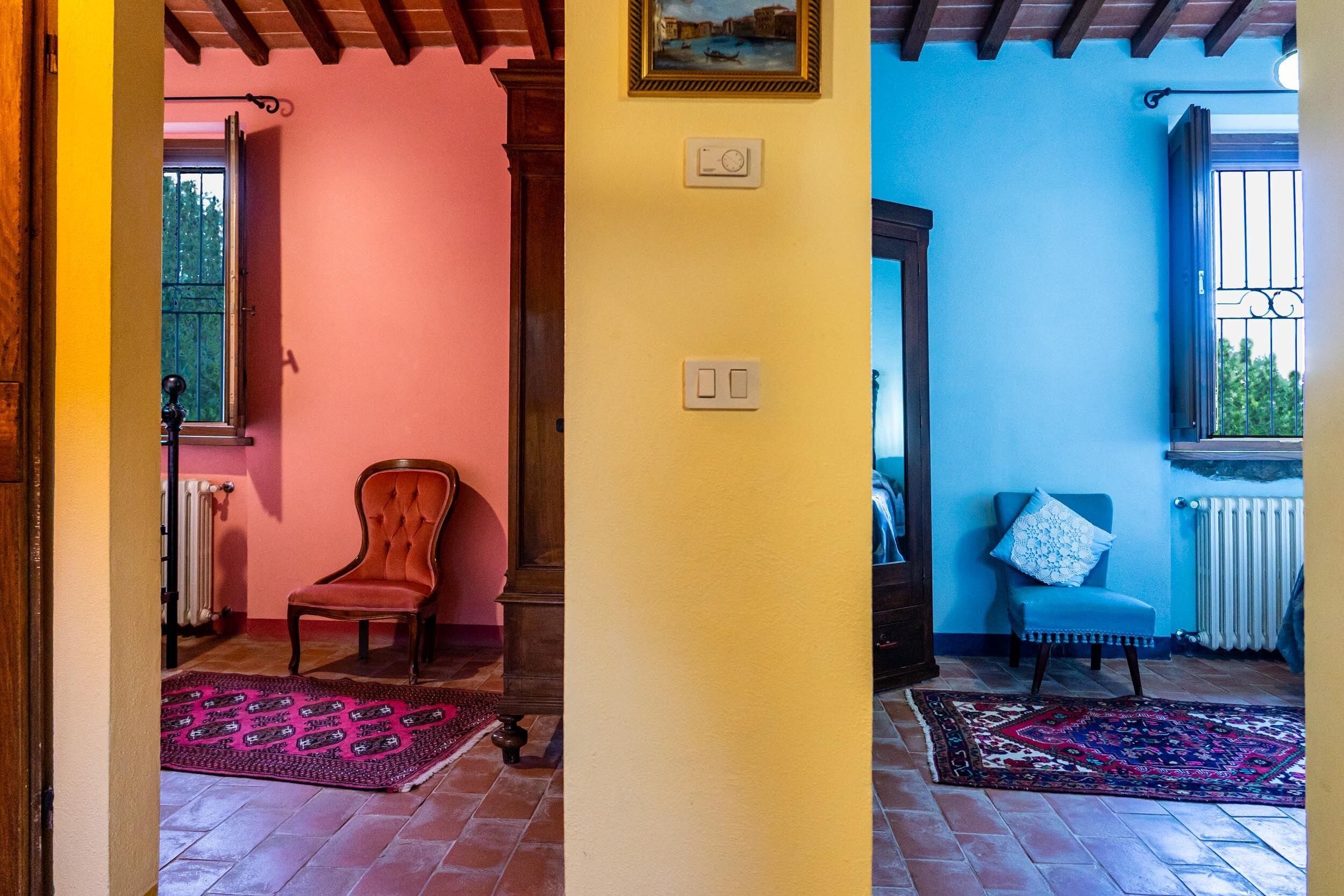 A room with a wooden floor, a red chair, a blue chair, and a patterned rug.