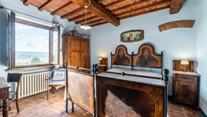 A bedroom with a wooden bed, a window with a view, a radiator, and a wooden cabinet. - Agriturismo il Querciolo (Marciano della Chiana)
