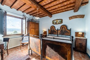 A bedroom with a wooden bed, a window with a view, a radiator, and a wooden cabinet. - Agriturismo il Querciolo (Marciano della Chiana)