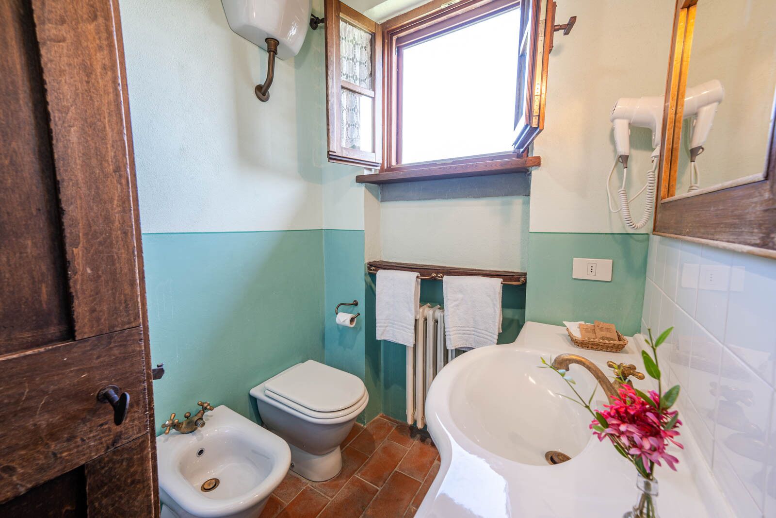 Un baño con bidé, inodoro, lavabo y ventana.