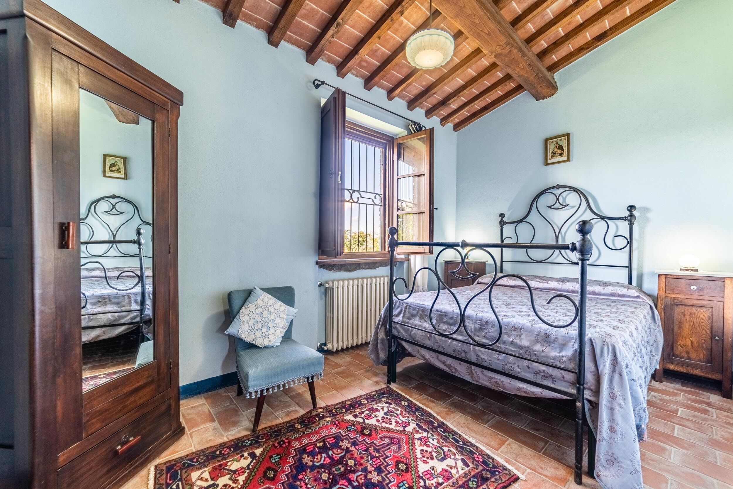 A bedroom with a bed, a chair, a wardrobe, a radiator, and a window.