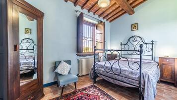 A bedroom with a bed, a chair, a wardrobe, a radiator, and a window.