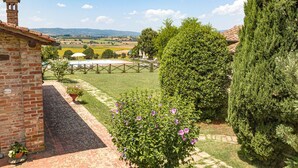A brick building with a tower, a well-maintained lawn, and a view of distant fields. - Agriturismo il Querciolo (Marciano della Chiana)